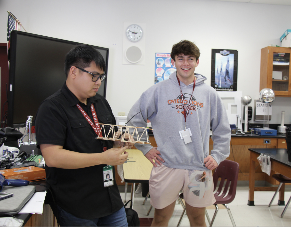 Science teacher Kier Tarrazona and physics club president Evan Mazzilli show an example bridge. The bridges were made out of popsicle sticks, skewer sticks, hot glue and tape.